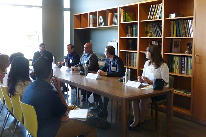 An audience of students attending a panel of speakers at a table in front of a bookshelf
