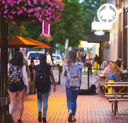 Students with backpacks walking on a lit sidewalk in dowtown Eugene