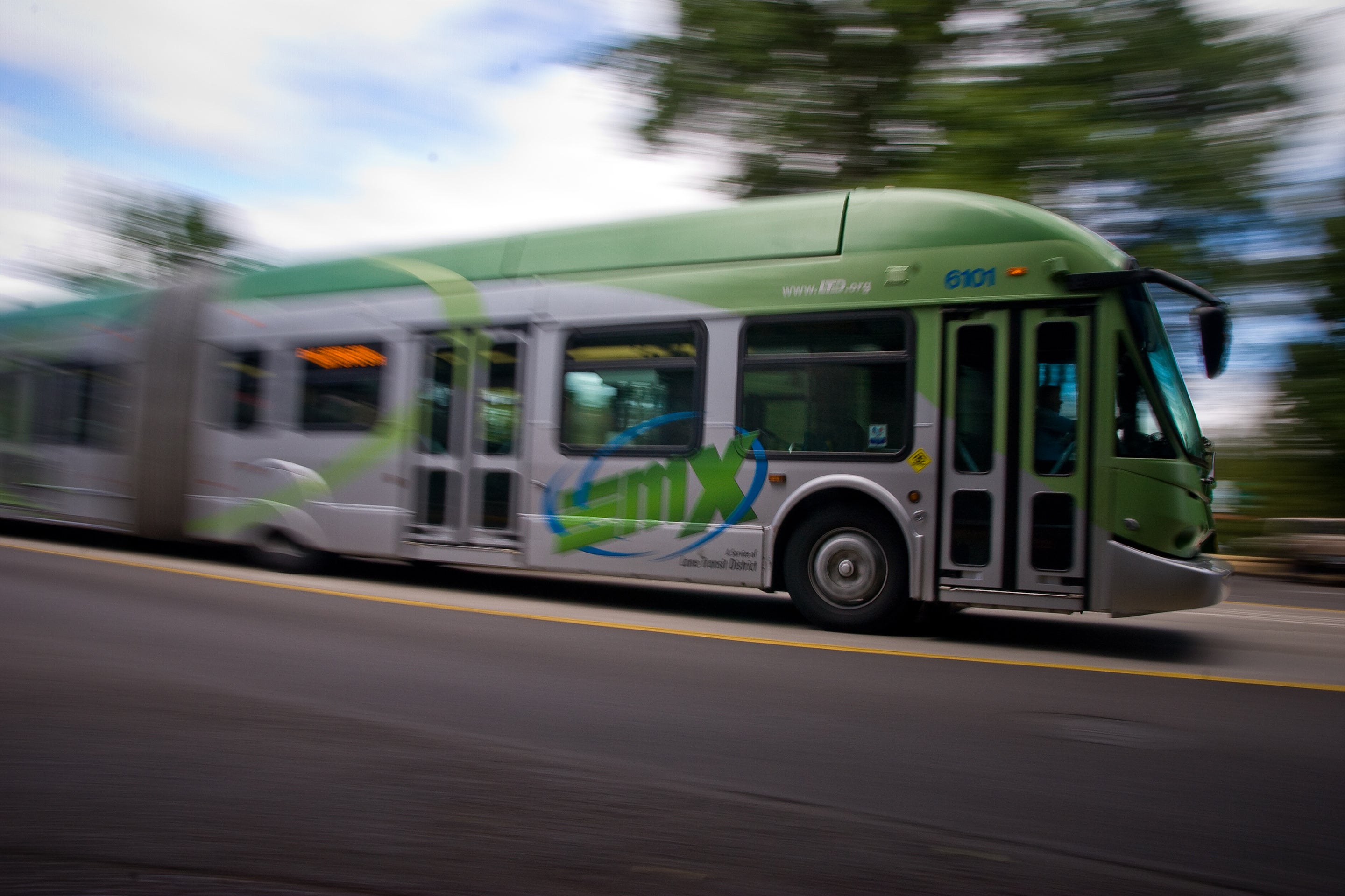Green articulated bus in motion to the right