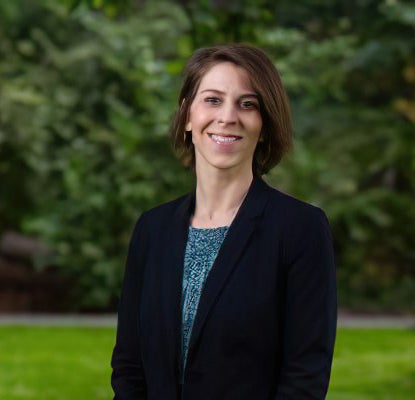 Dr. Lesley Jo Weaver standing on a grass lawn, pine trees in the background.