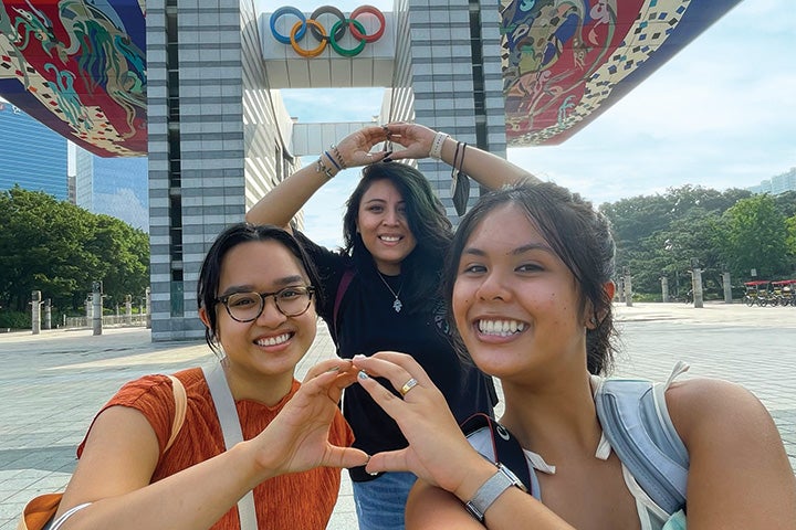 Three students throwing O's in front of an Olympic sign in Seoul