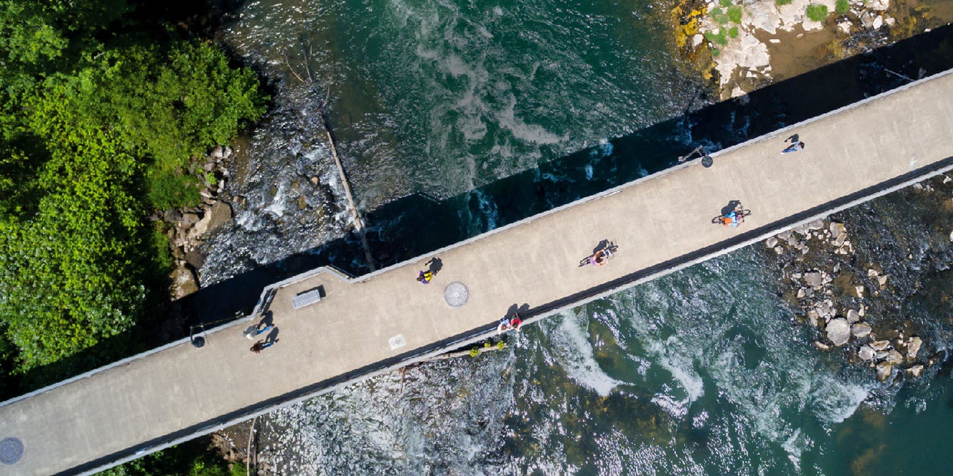 An aerial view of pedestrians and cyclists crossing the Autzen footbridge over the Willamette River near campus.