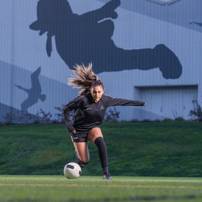 Student wearing a black 'Oregon' uniform plays soccer on the intramural fields nestled between the Student Recreation Center and Hayward Field.