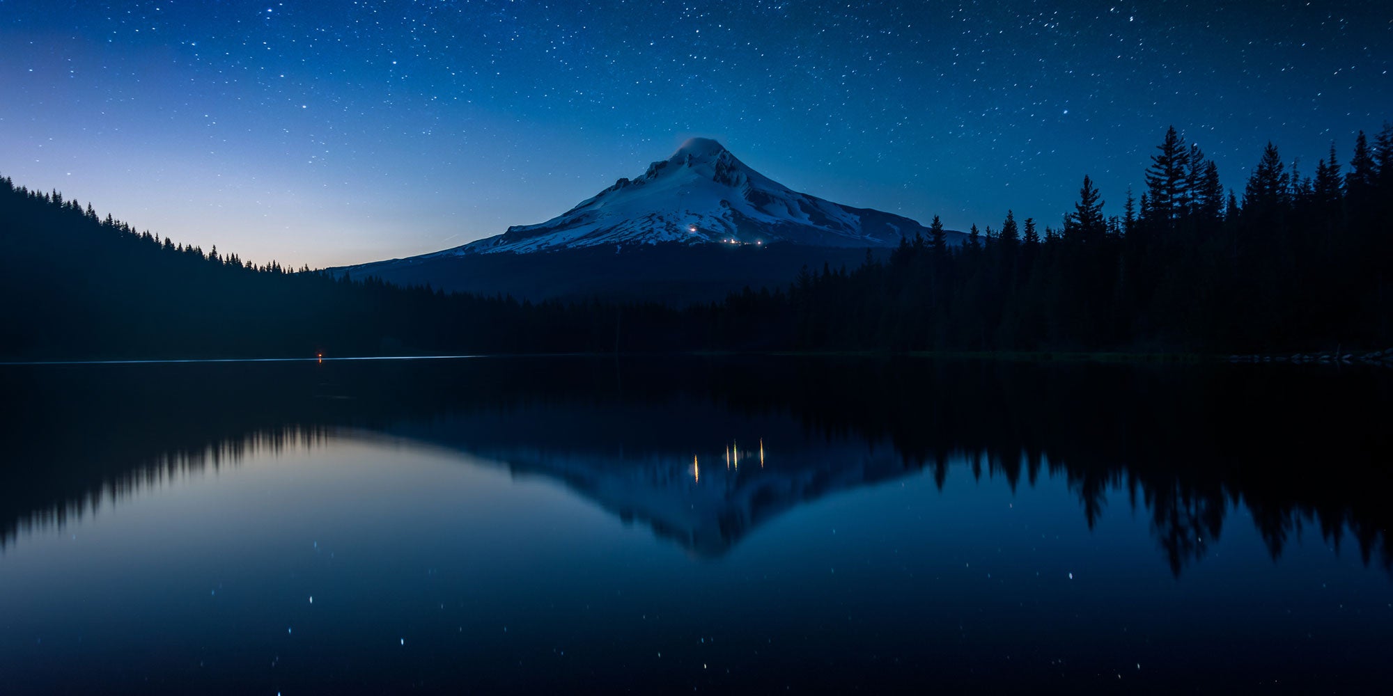 Nighttime view of a conical volcano mountain mirrored in an alpine lake