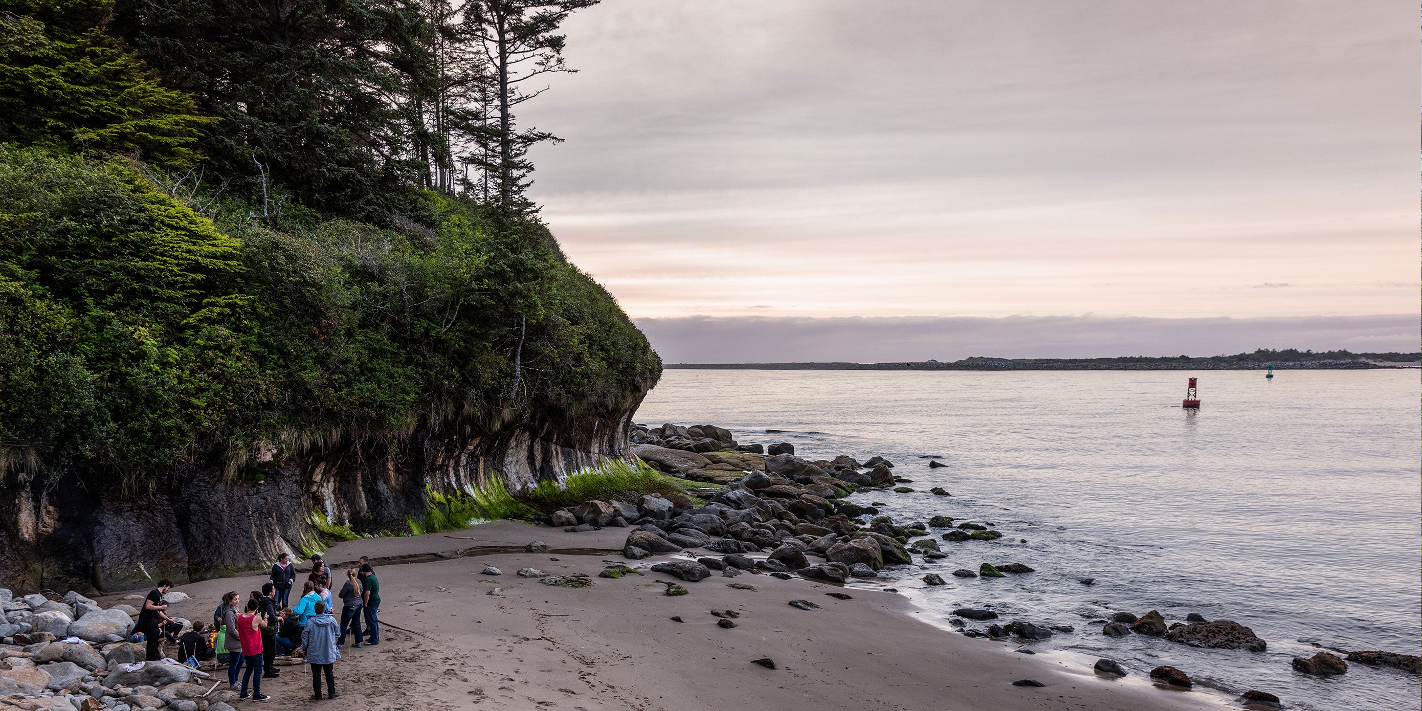 A group of students on a rocky beach under forested cliff face