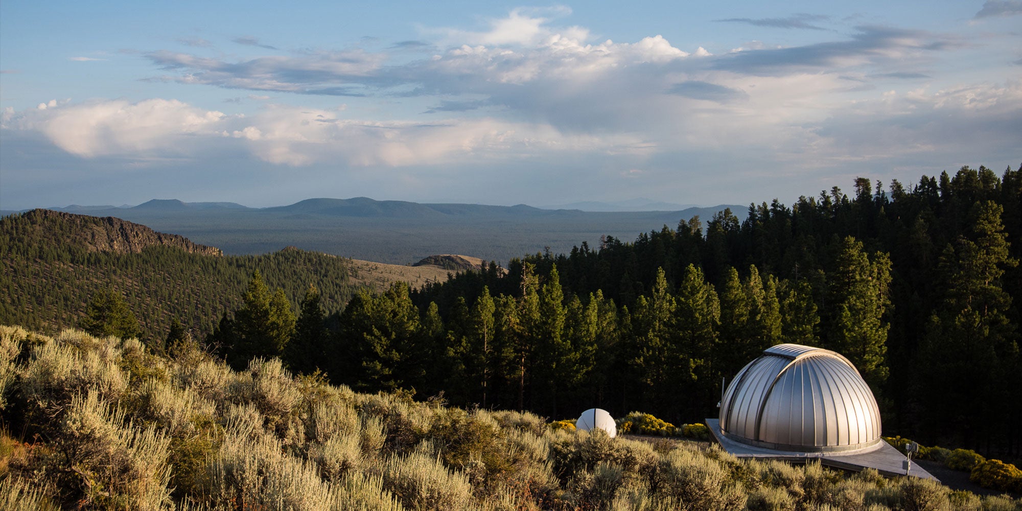 An observatory dome is surrounded by forested hills.